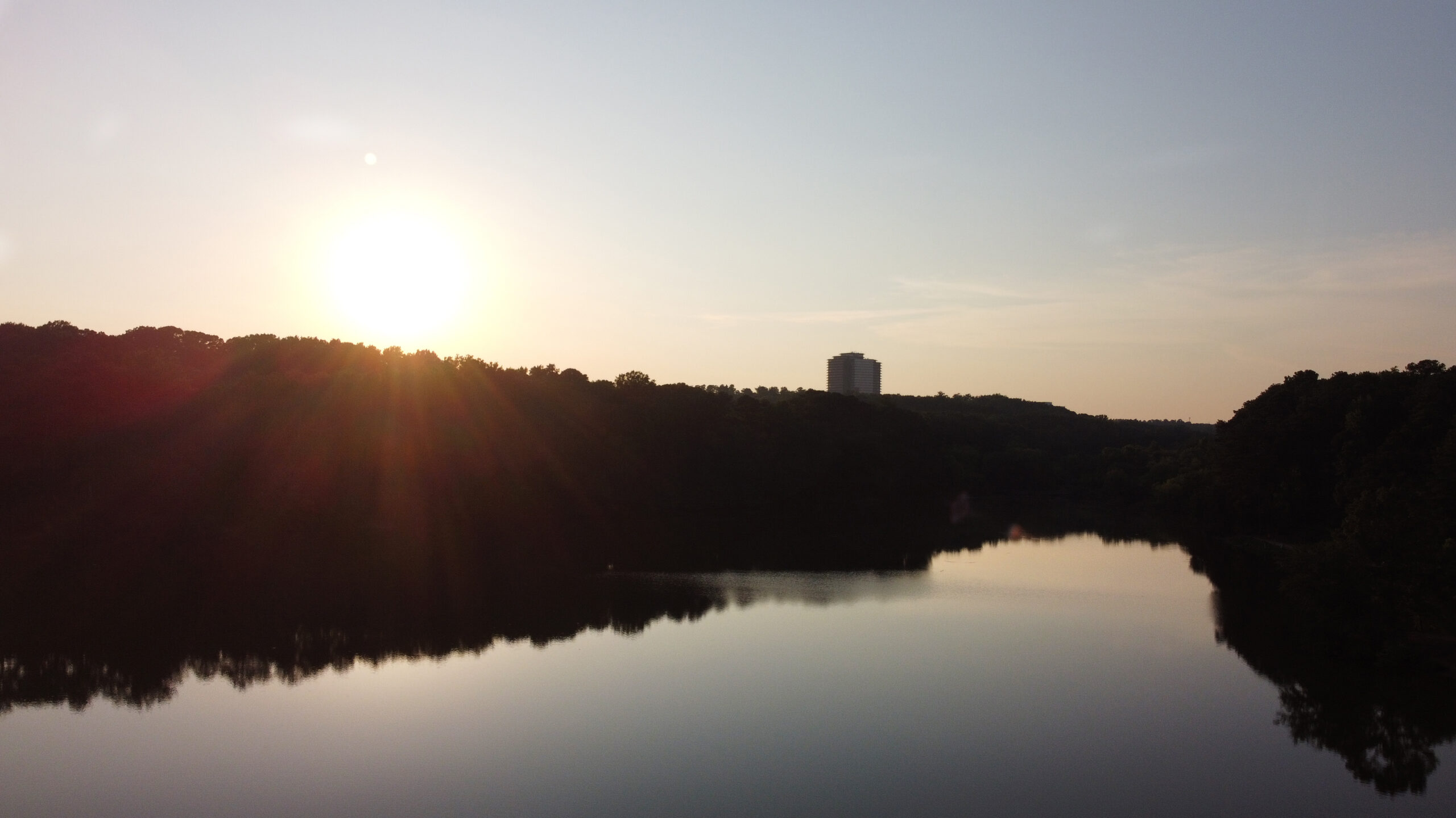 Drone aerial view of water and surrounding trees with an office building in the distance, representing real estate visual media.